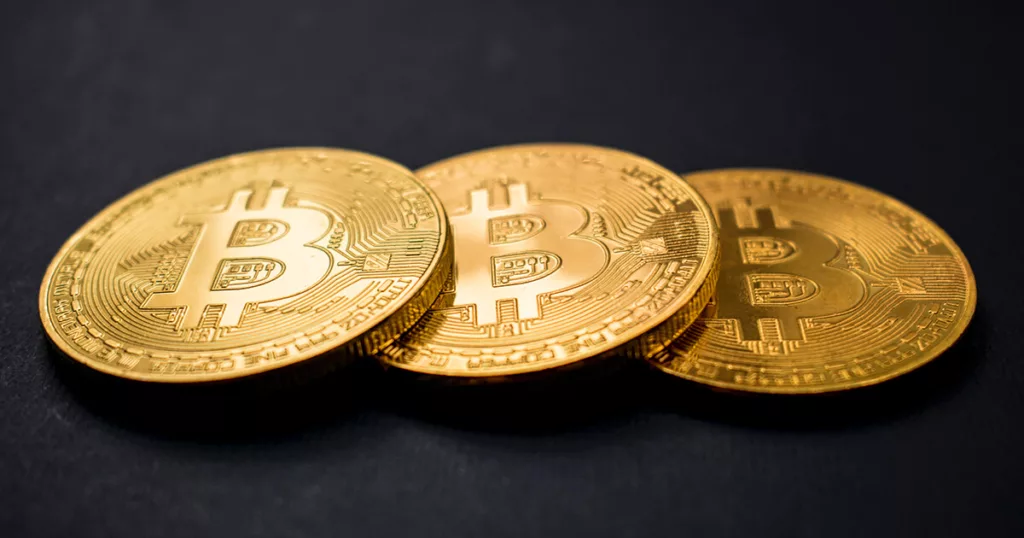 Three Gold color Bitcoin cryptocurrency placed on a black surface.